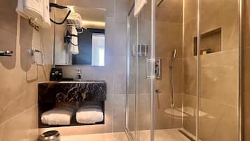 Un baño moderno con ducha envuelta en vidrio, paredes de azulejos de mármol, lavamanos empotrado con encimera de mármol y toallero con varias toallas.