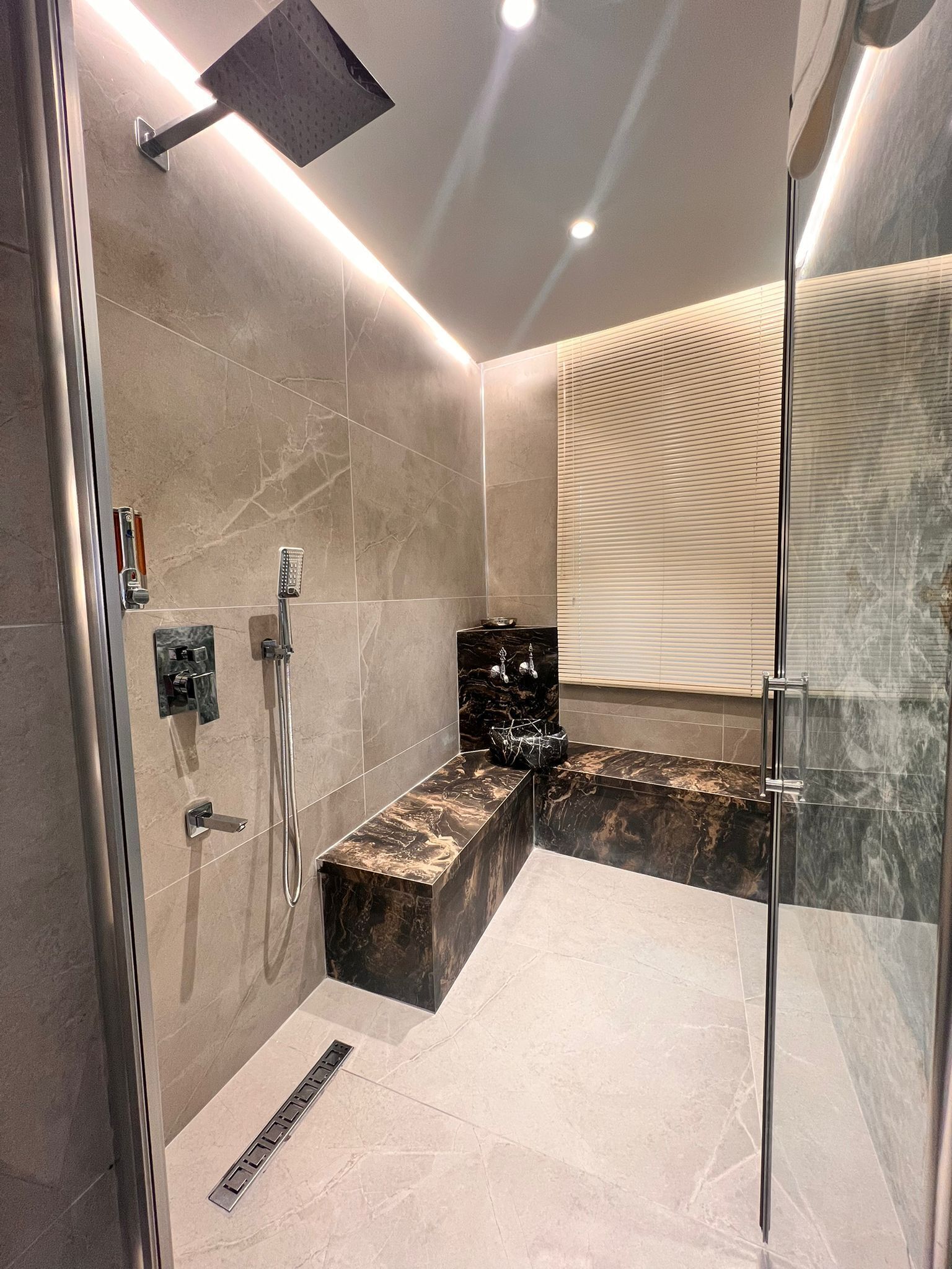 A modern bathroom with a glass shower enclosure, marble tiles, and a built-in bench.