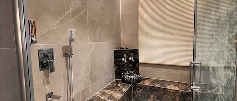 A modern bathroom with a glass shower enclosure, marble tiles, and a built-in bench.