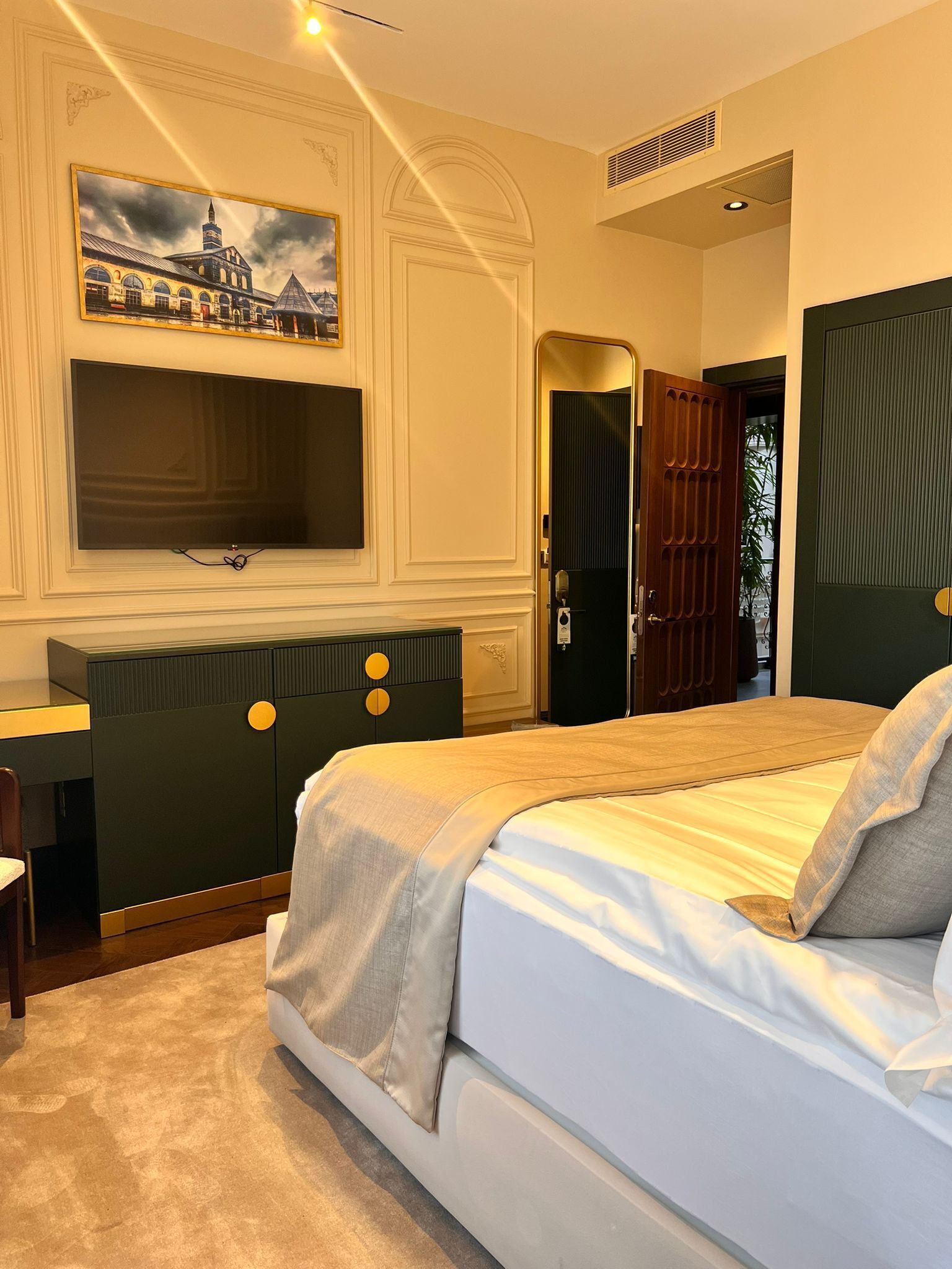 A bedroom with a bed, a desk, a television, and a painting on the wall.