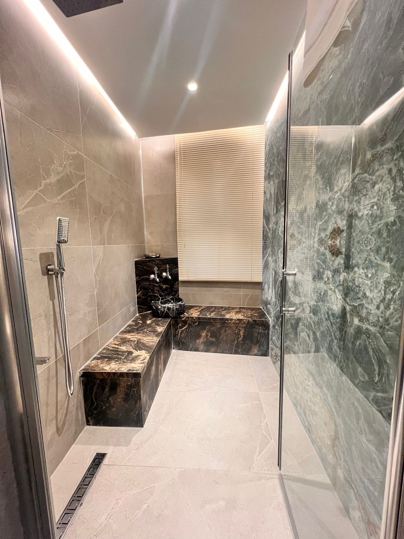 A modern bathroom with a glass shower enclosure, marble tiles, and a bench.