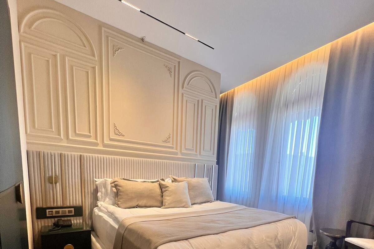 A bedroom with a large bed, a nightstand, a chair, and a window with curtains.