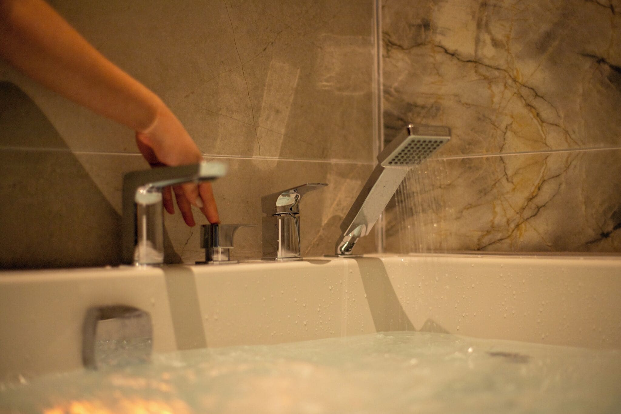 Une baignoire dotée de plusieurs robinets et d’une pomme de douche, le tout installé devant un mur de marbre.