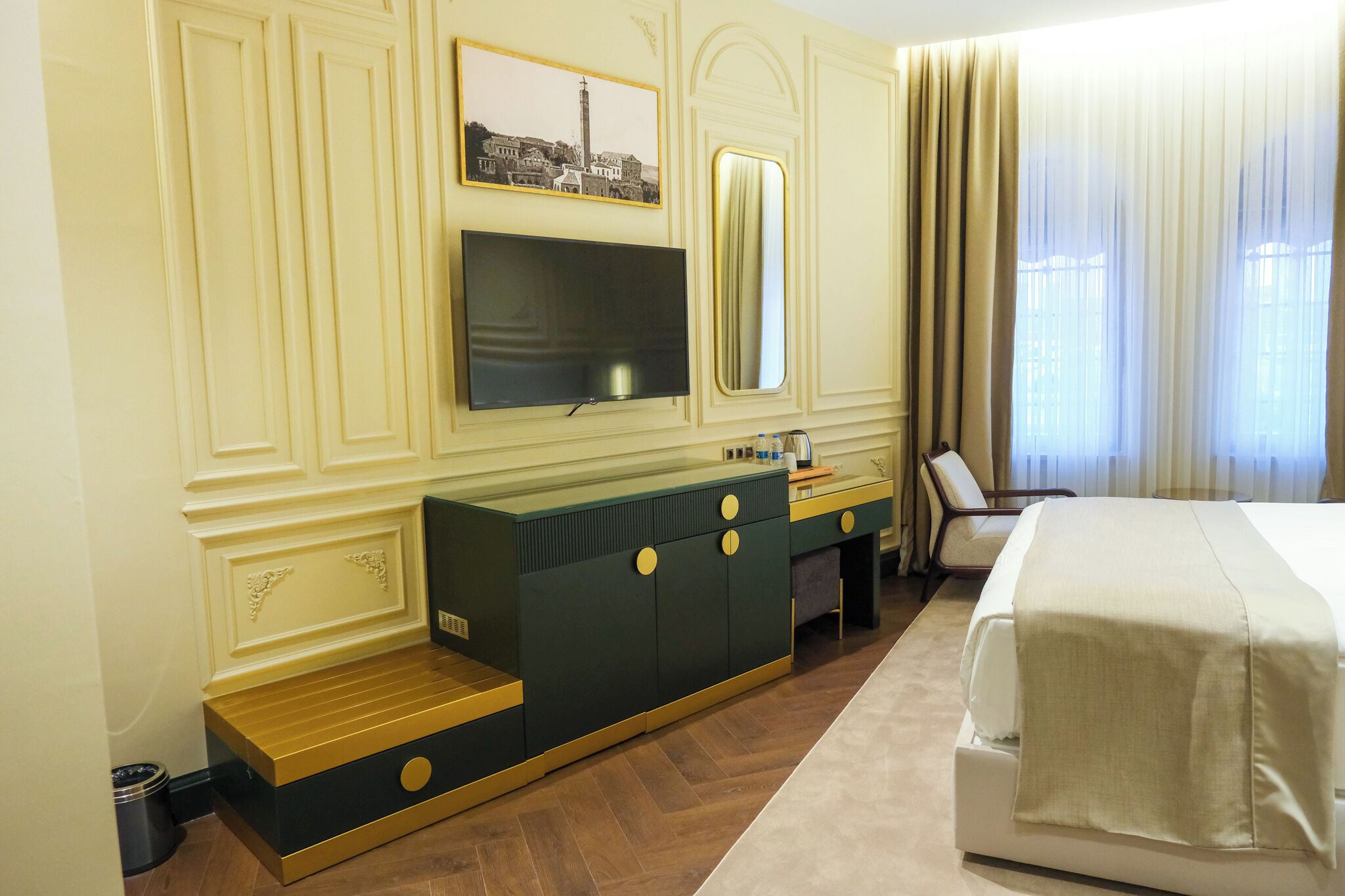 A hotel room with a large bed, a TV mounted on the wall, a minibar, and a window with curtains.