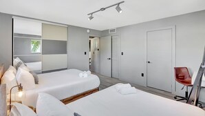 A modern hotel room with two beds, a desk, a chair, and a large window. - Newly Renovated 1BR Condo Near South Beach (Miami Beach)