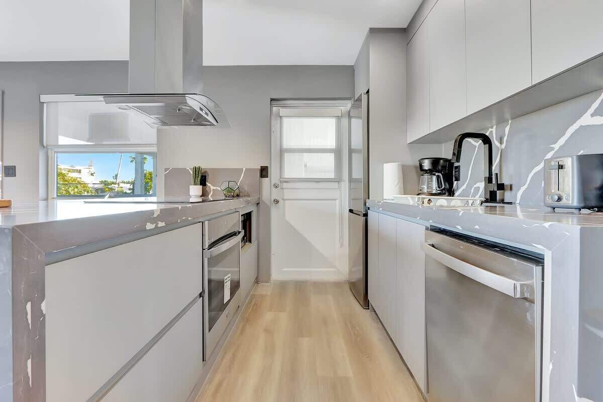 A modern kitchen with stainless steel appliances, a view through an open door, and a clean, minimalist design.
