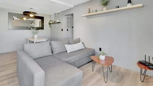 A modern living room with a grey sectional sofa, a small round coffee table, and a white side table with a vase. - Newly Renovated 1BR Condo Near South Beach (Miami Beach)