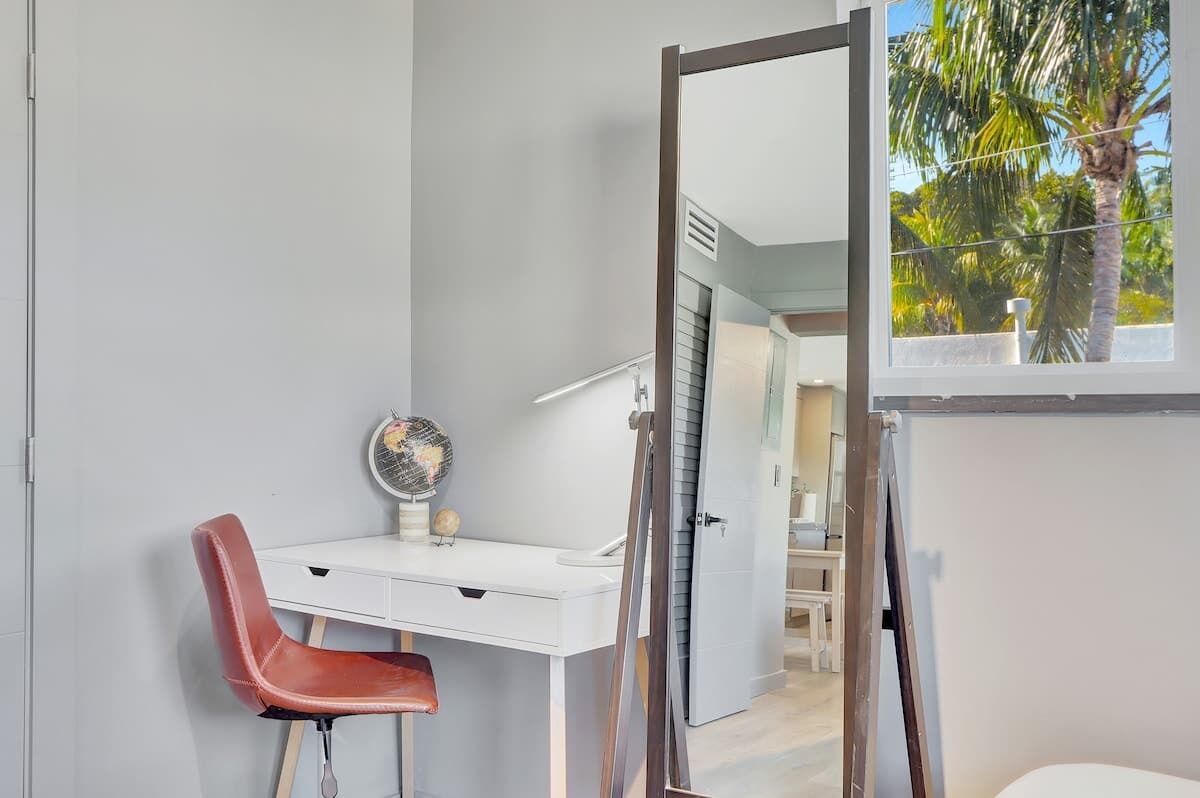 A room with a white desk, a red chair, a globe, and a window with a view of palm trees.