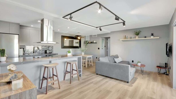 A modern kitchen with a central island, bar stools, and a grey sofa in a living area with a wooden floor. - Newly Renovated 1BR Condo Near South Beach (Miami Beach)