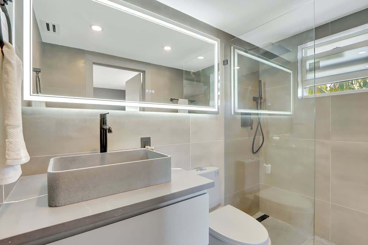 Un baño moderno con un lavamanos rectangular, un inodoro y una ducha con cerramiento de vidrio.