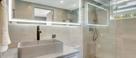 Un baño moderno con un lavamanos rectangular, un inodoro y una ducha con cerramiento de vidrio.