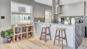 A modern kitchen with a central island, bar stools, and a built-in bookshelf. - Newly Renovated 1BR Condo Near South Beach (Miami Beach)