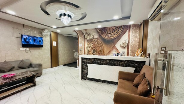 A modern living room with a marble floor, a brown sofa, a grey sofa, a TV mounted on the wall, and a decorative wall panel. - Hotel S.R. Plaza (New Delhi)