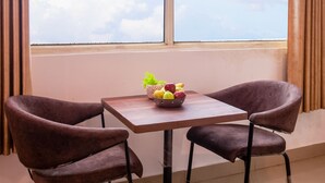 A room with a large window, a table with a bowl of fruit, and two chairs. - Hotel S.R. Plaza (New Delhi)