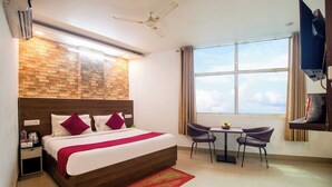 A hotel room with a large bed, a small table with chairs, a TV, and a window with a view. - Hotel S.R. Plaza (New Delhi)