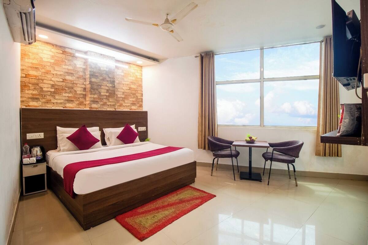 A hotel room with a large bed, a small table with chairs, a TV, and a window with a view.
