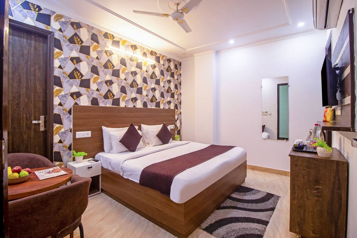 A modern bedroom with a wooden bed, a nightstand, a desk with a chair, and a wall-mounted TV.