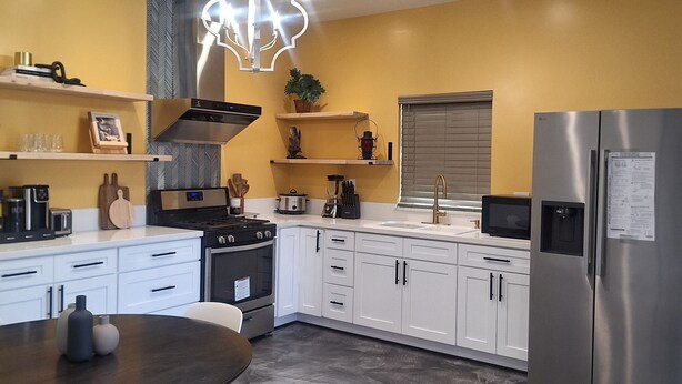 A modern kitchen with white cabinets, a stainless steel refrigerator, and a dining area with a round table and chairs.