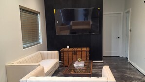 A modern living room with a white sofa, a coffee table with books, and a large mirror on the wall.