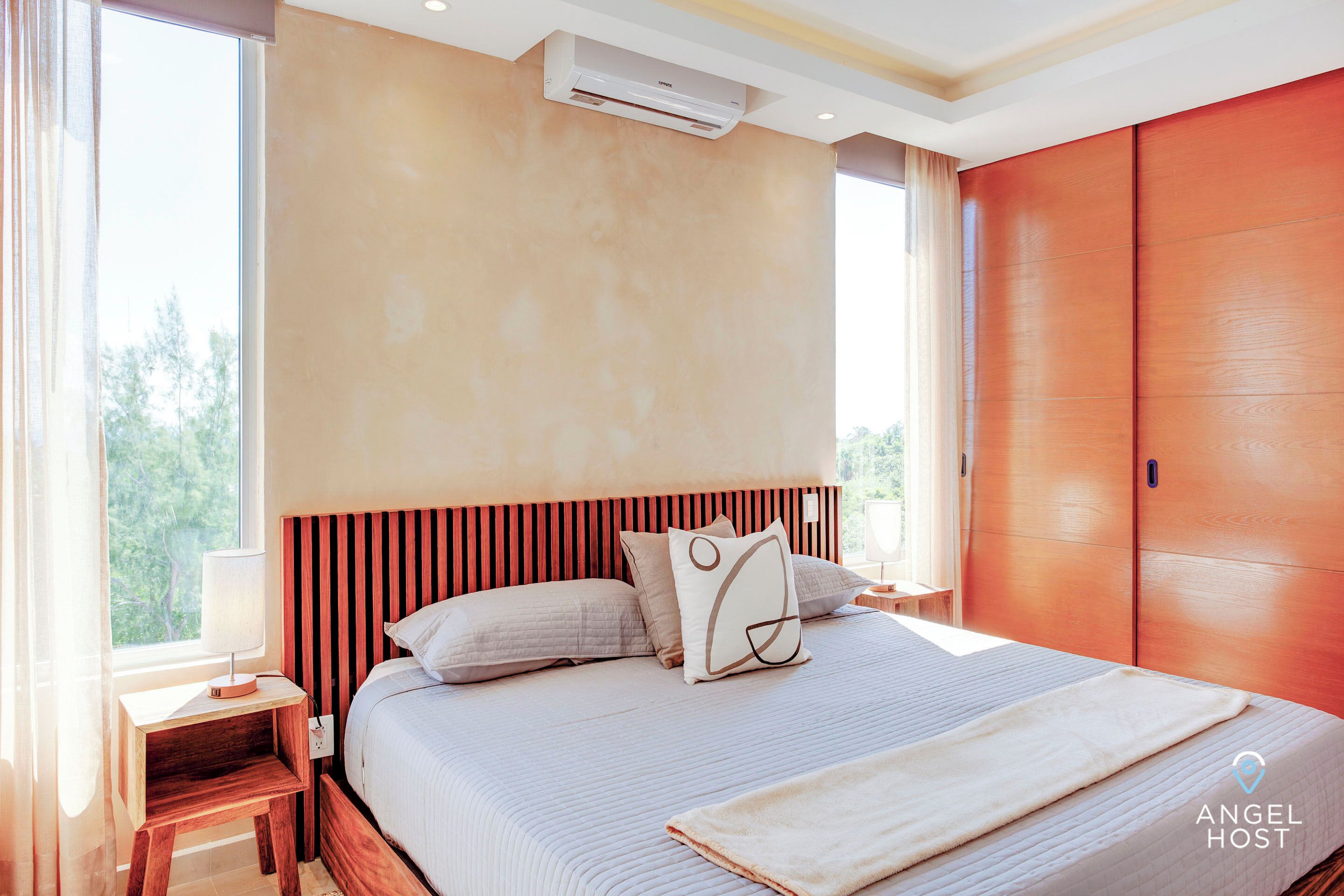 A bedroom with a large bed, a nightstand, a wall-mounted air conditioner, and a window with curtains.