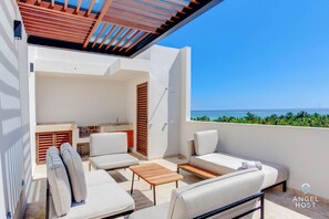 A balcony with a sofa, a table, and a view of the sea. - Jungle & Ocean View Condos (Playa del Carmen)
