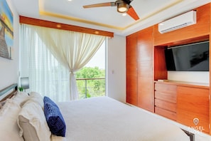 A bedroom with a bed, a ceiling fan, a TV, and a window with curtains.
