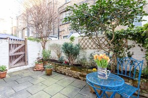 A courtyard with a blue metal table and chair, surrounded by potted plants and a white wall. - Cosy Pimlico Retreat (London)