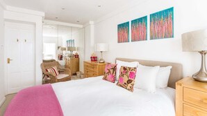A hotel room with a bed, a nightstand, a lamp, a chair, a dresser, and artwork on the wall. - Cosy Pimlico Retreat (London)