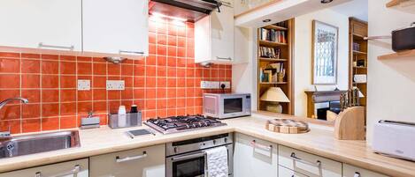 A kitchen with white cabinets, an orange-tiled backsplash, a gas stove, a microwave, and a toaster.