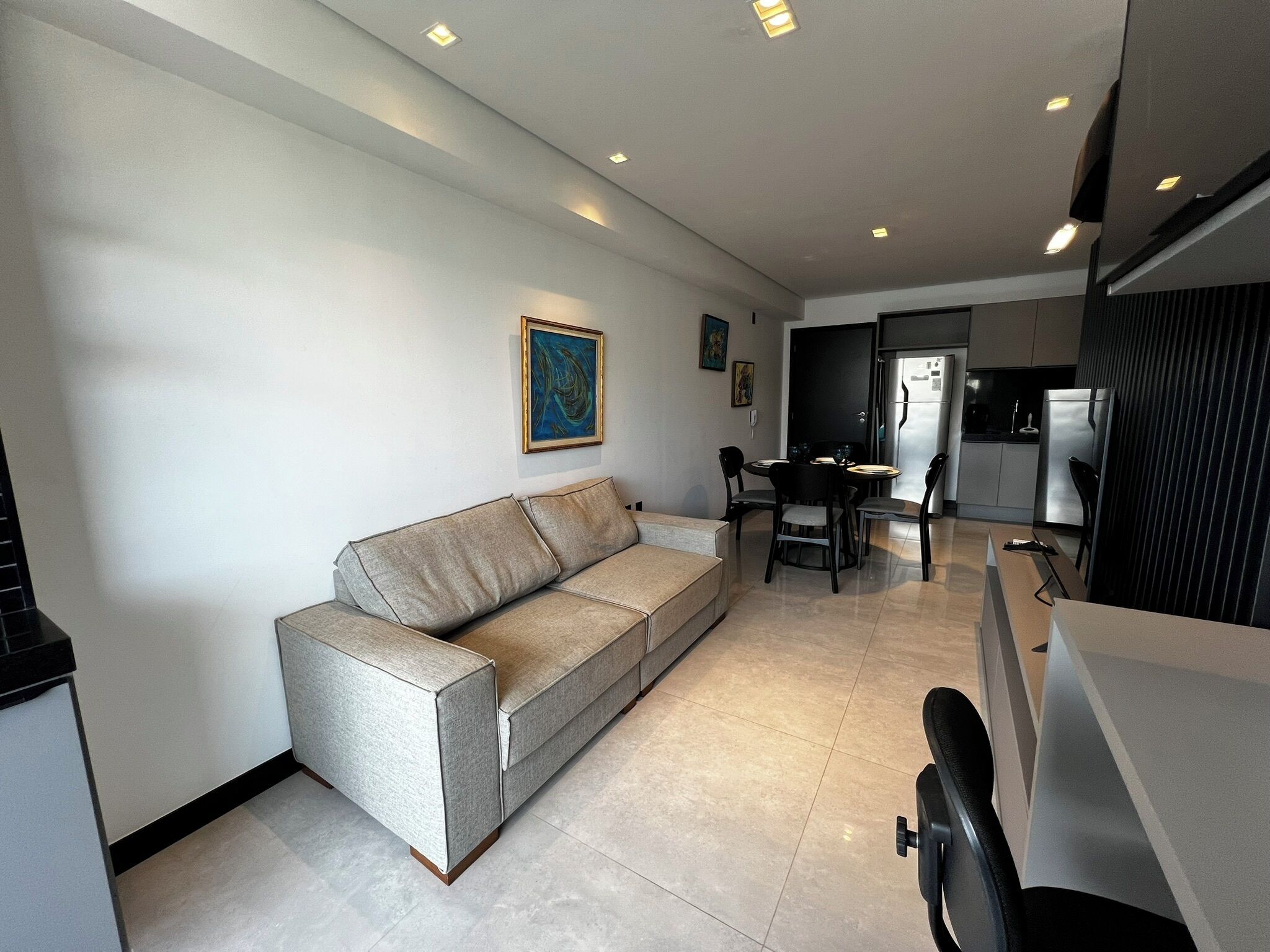 Una sala de estar moderna con un sofá, una mesa de comedor, sillas y una zona de cocina con un refrigerador.