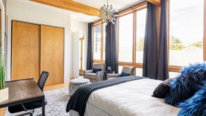 A modern hotel room with a large bed, a desk, and a chair. There are large windows with curtains, a chandelier, and a view of the outside. - Uniquely Nashville, this Property has Amazing Views, A great Location to Unwind (Nashville)