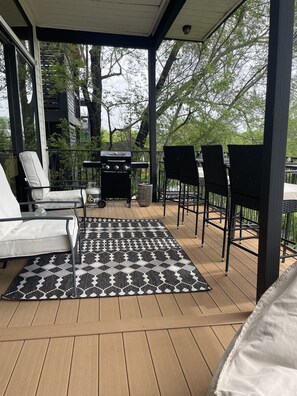 An outdoor patio with a grill, seating, and a view of trees.