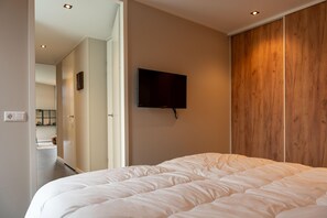 Une chambre à coucher avec un grand lit, un téléviseur fixé au mur et une armoire en bois.