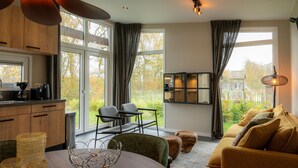 Eine moderne Küche mit großen Fenstern, ein Essbereich mit einem runden Tisch und ein gemütliches Wohnzimmer mit einer Couch und Hocker.