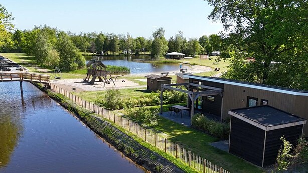 Ein Anwesen am Flussufer mit einer Holzbrücke, einem Pavillon und einem kleinen Gebäude.