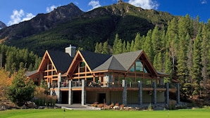 A lodge with a stone foundation and wooden beams, featuring large windows and a balcony overlooking a golf course. - Spacious Toby Creek loft with river and mountain views (Panorama)