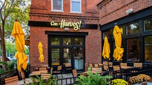 An outdoor seating area with yellow umbrellas and wooden tables, a brick building with a sign reading "Con Huevos!" - Pet Friendly, Pool, Shops, Downtown, Bourbon, Golf Local Dining, Fully Loaded (Prospect)