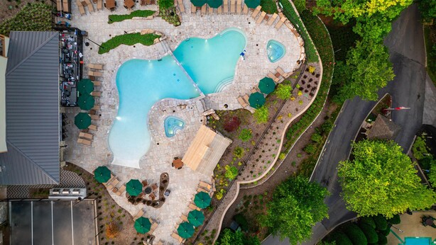 An aerial view of a resort with two swimming pools, outdoor seating areas, and landscaped gardens.