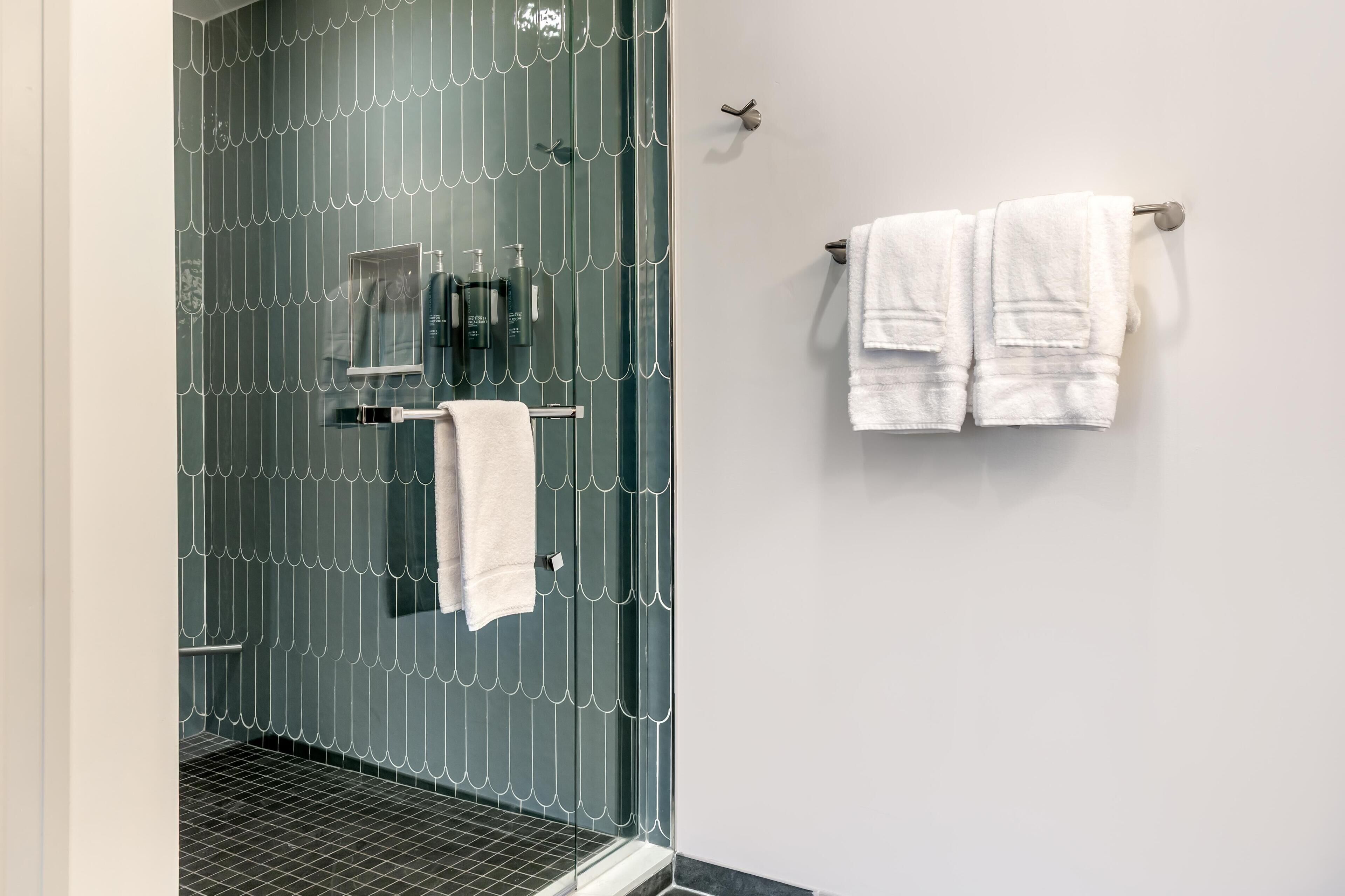 A bathroom with a glass shower enclosure, a towel rack with two white towels, and a mirror.