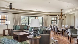 A modern living room with a sectional sofa, a dining area with a table and chairs, and large windows with curtains.