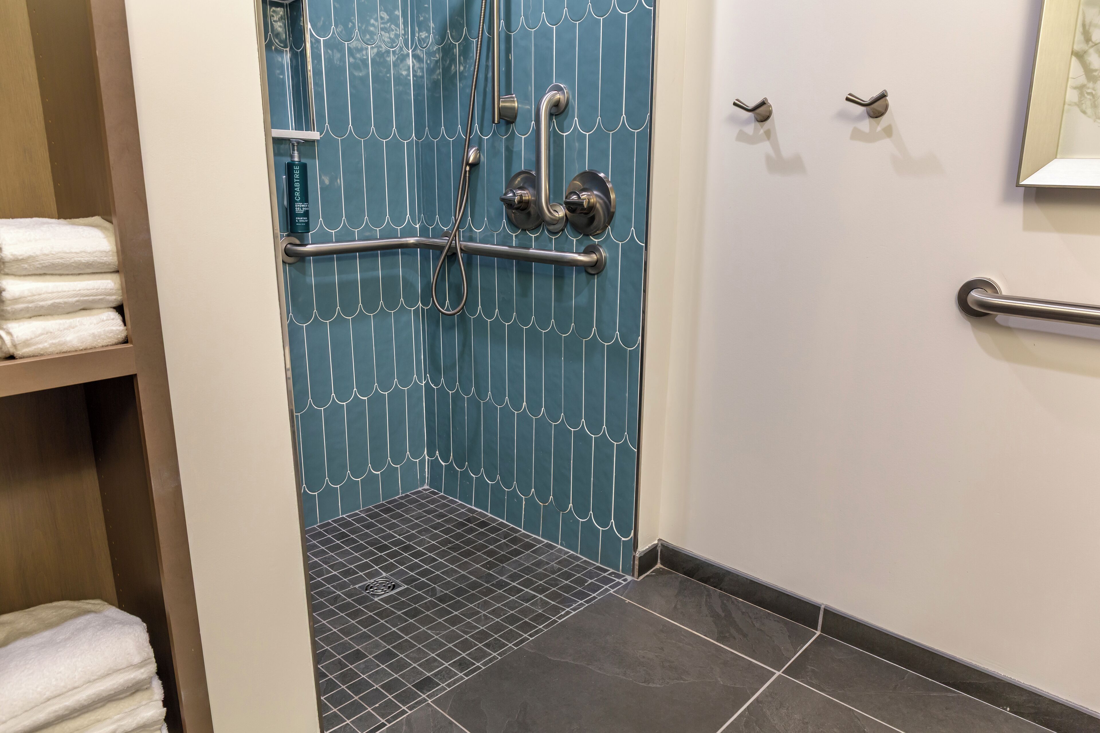 A bathroom with a blue tiled shower enclosure, a grab bar, a towel rack, and a hand dryer.