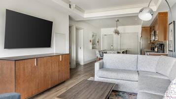 Uma sala de estar moderna com uma televisão de tela plana grande, uma mesa de centro de madeira e um sofá modular cinza.