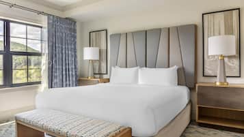 A hotel room with a large bed, bedside tables with lamps, a bench, and a view of the outdoors.