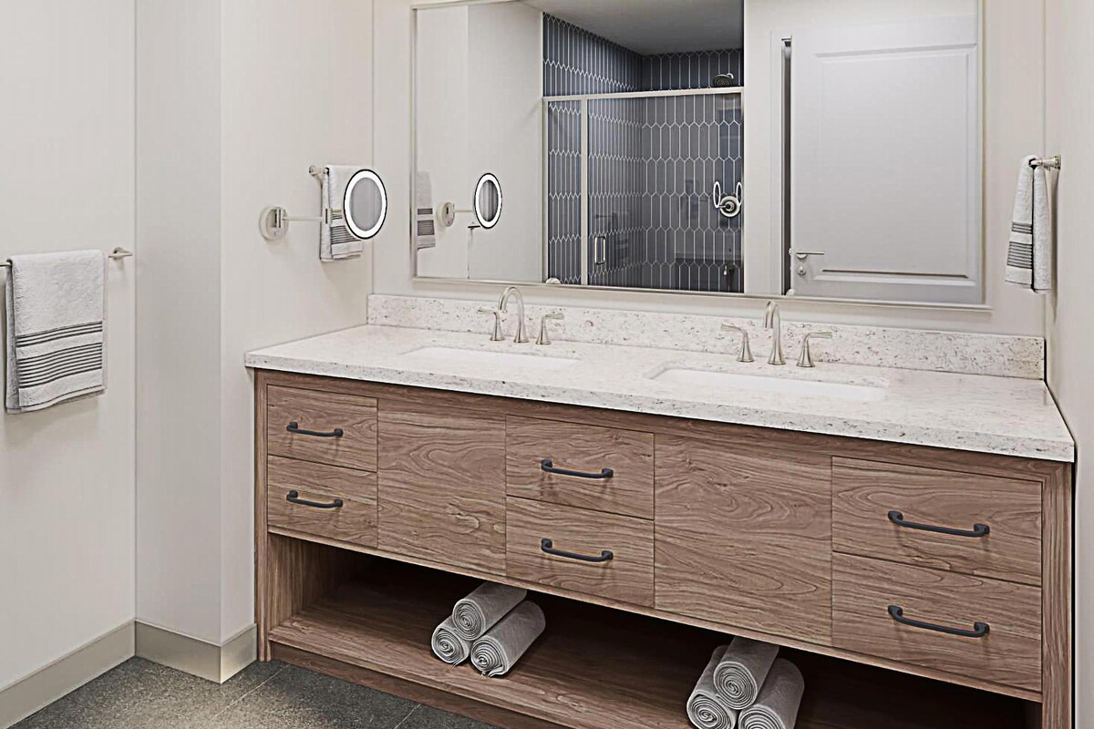 Un baño moderno con un espejo grande, dos lavamanos, tocador de madera y un perchero para toallas.