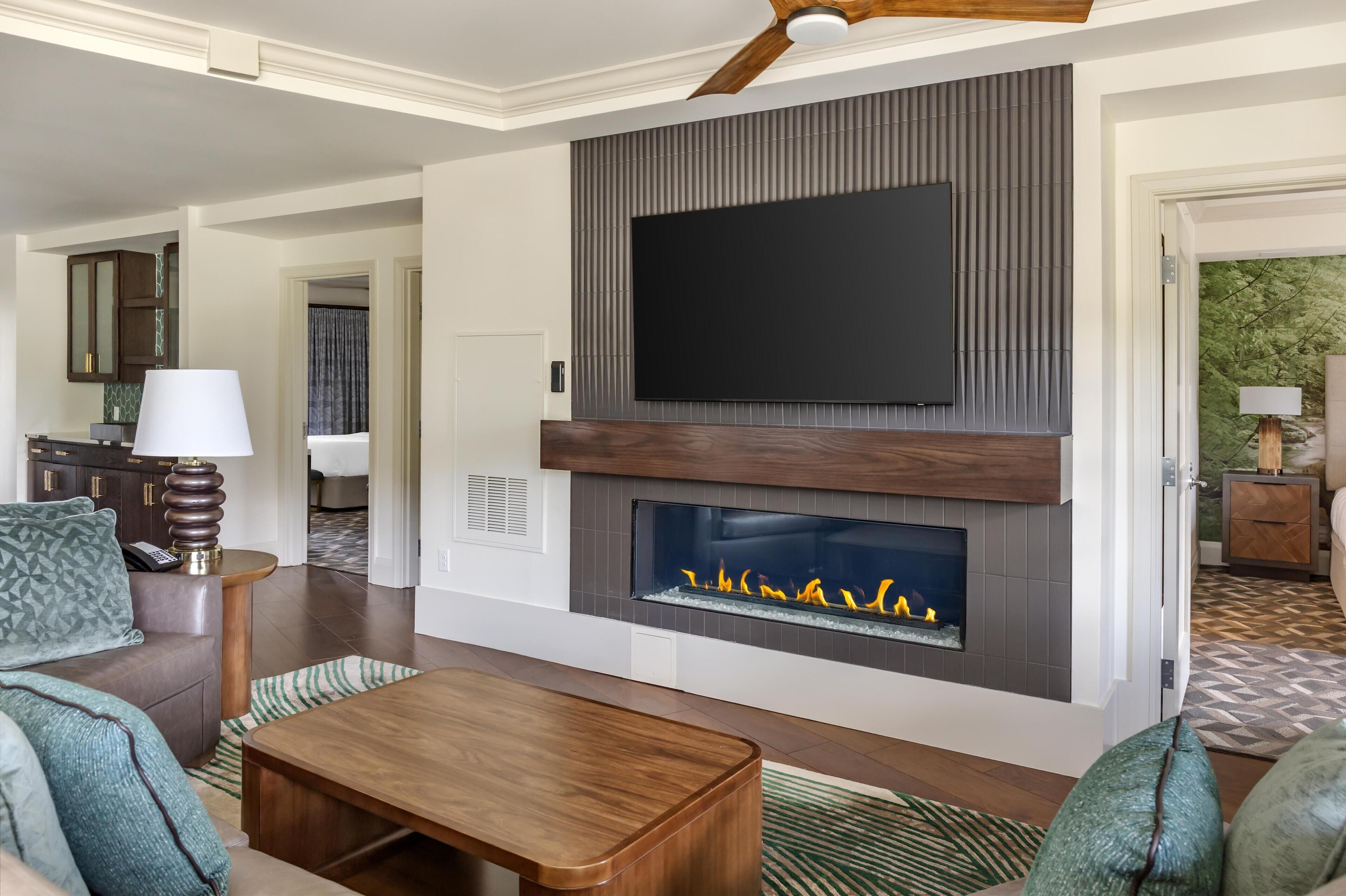 A modern living room with a fireplace, a flat-screen TV, and a dining area.