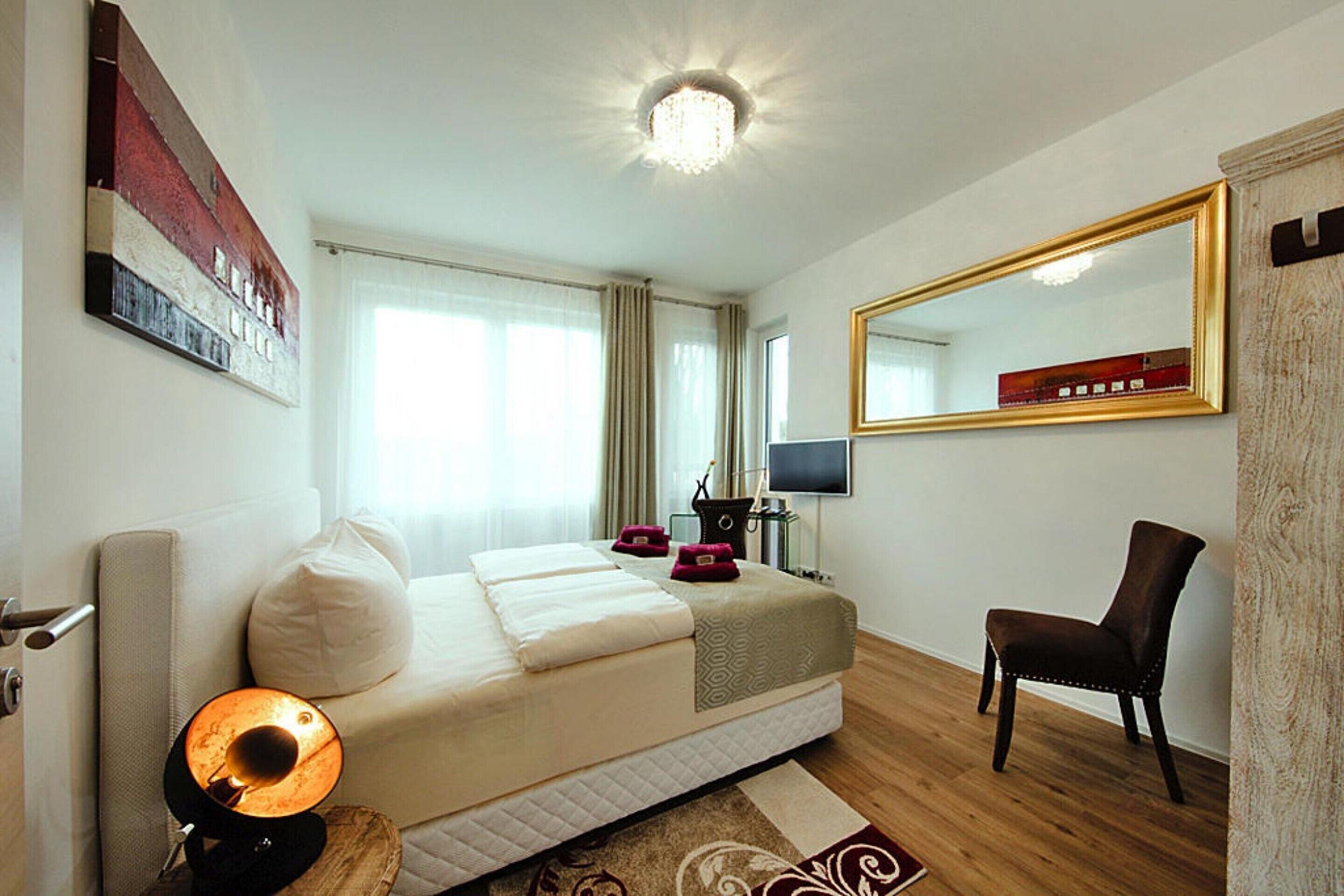 A hotel room with a bed, a chair, a TV, and a large mirror.