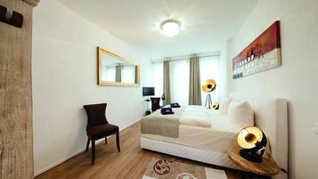 A hotel room with a bed, a chair, a desk, a lamp, and a painting on the wall.
