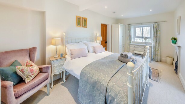 Een slaapkamer met een bed, nachtkastjes, een stoel, een kledingkast en een raam.