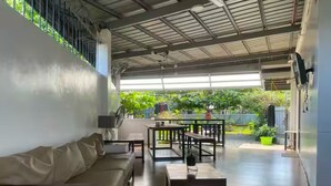 A modern living room with a sofa, tables, and a view of a lush garden. - 5BR House with Centralized AC, Backyard & Office (Roxas City)