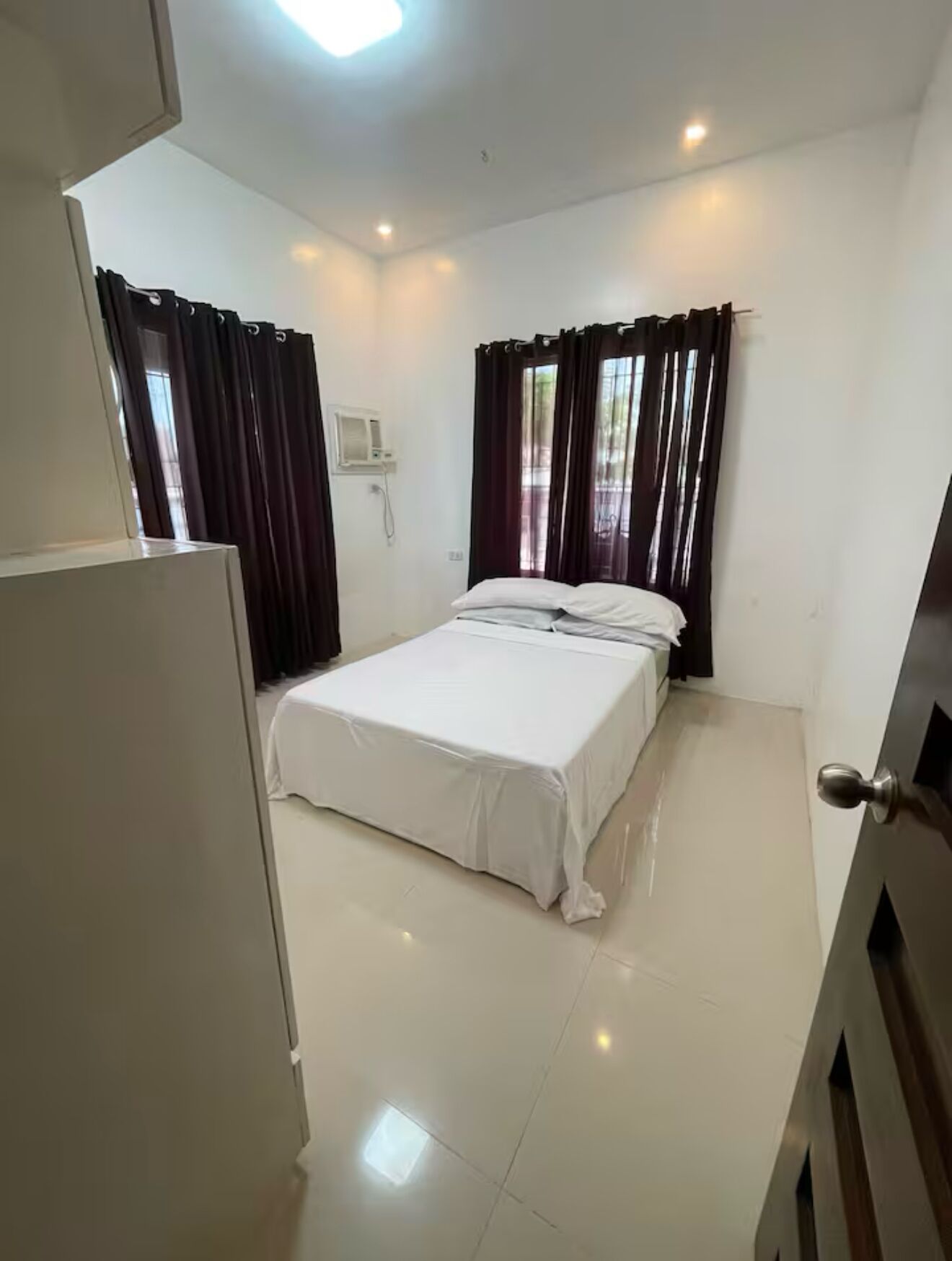 A bedroom with a bed, white walls, a ceiling light, and a window with curtains.